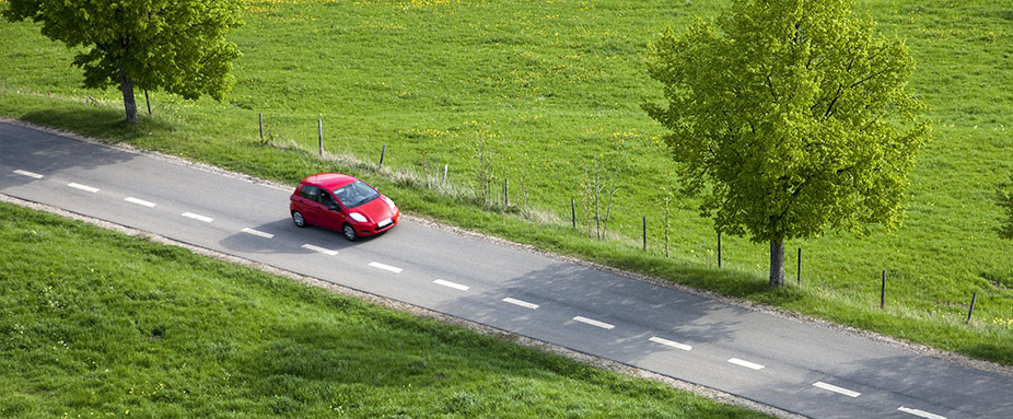 Rotes Auto fährt auf der linken Seite auf einer Landstraße.