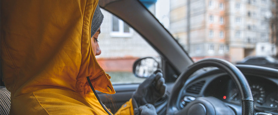 Frau sitzt mit Handschuhen im Auto und lässt Motor warm laufen