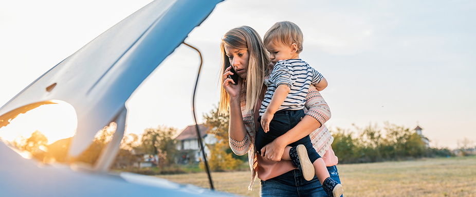 Frau mit Kind auf dem Arm schaut nach einer Panne in den Motorraum 