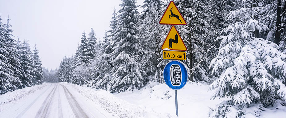 verschneite Straßen mit Straßenschild das auf Schneeketten hinweißt