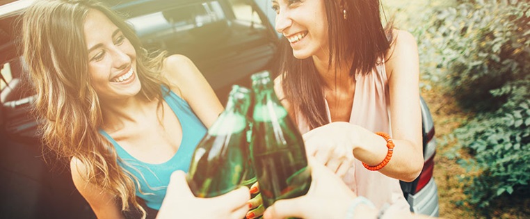 Zwei Frauen trinken Alkohol vor Auto