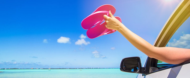 Frau hält pinke Flip-Flops aus Autofenster