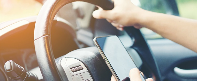 Mensch hält Handy bei der Autofahrt vors Lenkrad