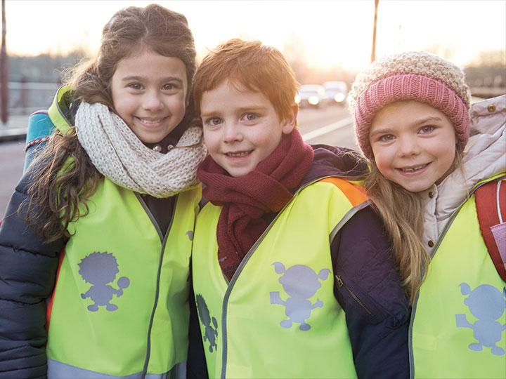 Schulkinder tragen Warnwesten und lachen in die Kamera