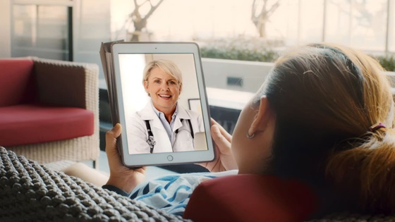 Frau betrachtet ein Tablet, auf dem eine Ärztin zu sehen ist