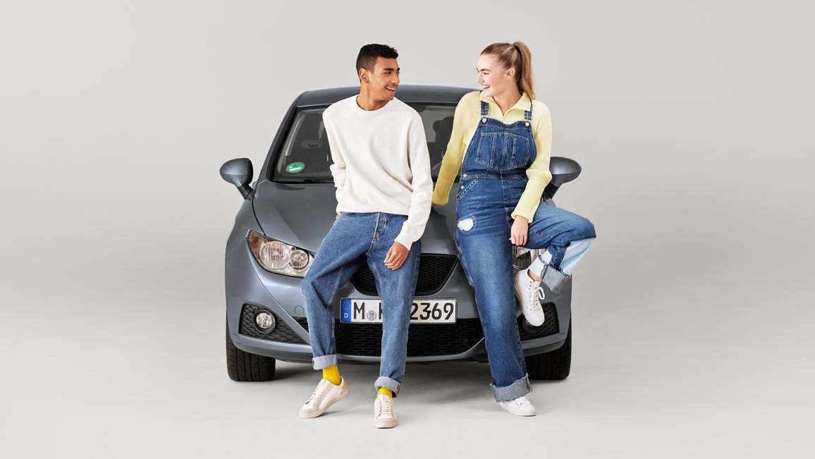 Zwei junge Leute sitzen auf der Motorhaube eines Autos und lachen