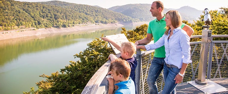 Eine Familie mit zwei Kindern genießt die Aussicht auf den Edersee auf dem Baumwipfelpfad Treetop Walk im Nationalpark Kellerwald
