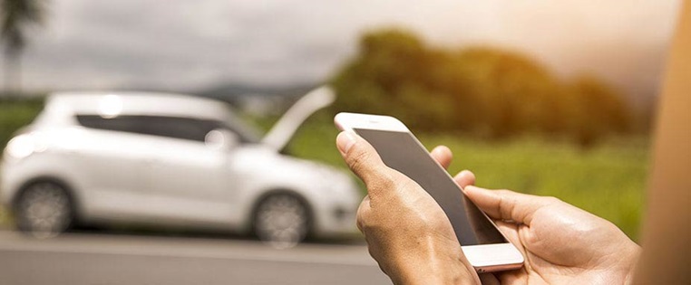 Frau steht mit einem Handy vor einem Pannenwagen
