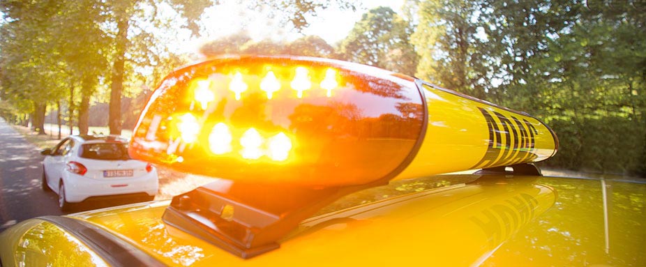 Großaufnahme vom gelben Warnlicht des Pannenhelfers, im Hintergrund das defekte Auto