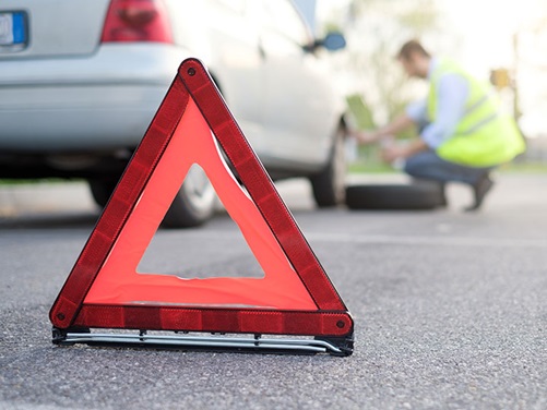 Warndreieck auf der Straße, im Hintergrund Auto mit Panne