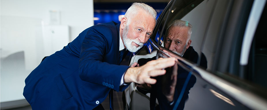 Älterer Herr schaut sich den Lack vom Auto genau an