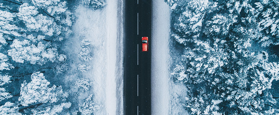 Luftaufnahme von einem Auto, dass auf einer Straße durch den verschneiten Wald fährt