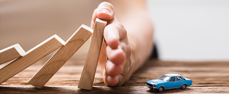 Hand hält Dominosteine aus Holz, damit sie nicht auf ein Spielzeugauto fallen