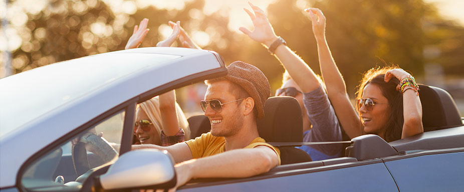 Junge Menschen sitzen jubelnd in einem Cabrio