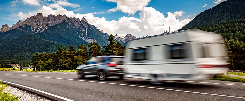 Auto mit Wohnanhänger fährt über eine Landstraße