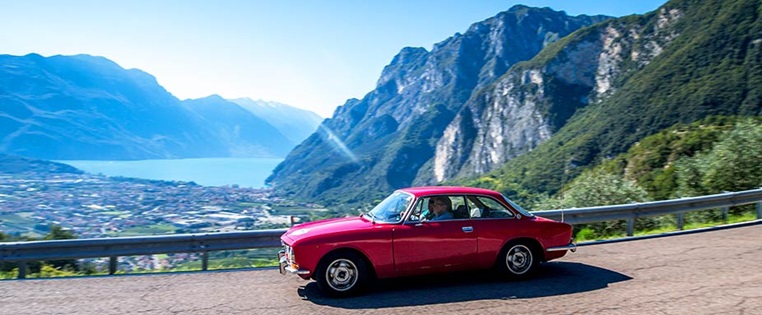 Oldtimer fährt auf Straße, See im Hintergrund