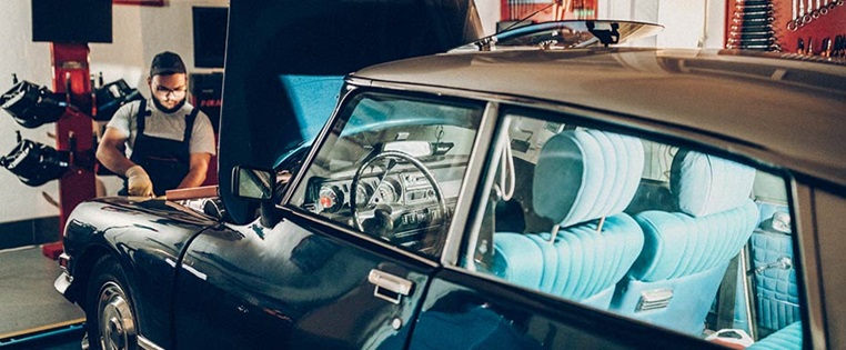 Dunkelblauer Oldtimer wird von einem Mann in Garage begutachtet Restauration