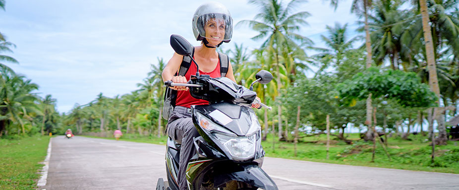 Eine Frau fährt auf einem Roller auf einer Strasse in Thailand