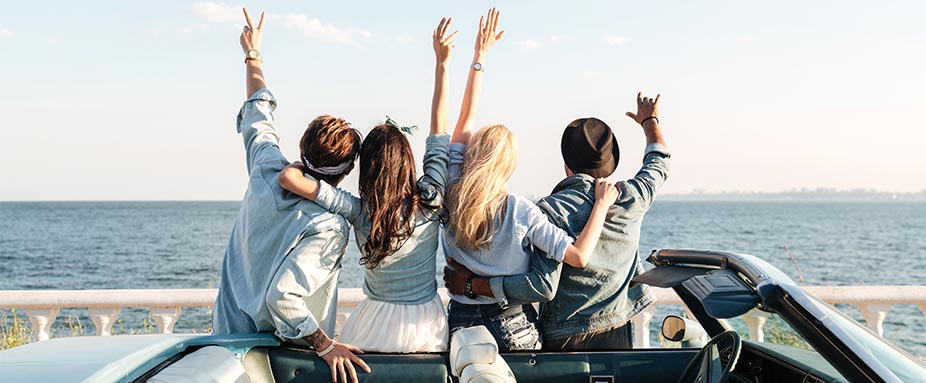 Junge Menschen stehen hinter Cabrio und haben Spaß