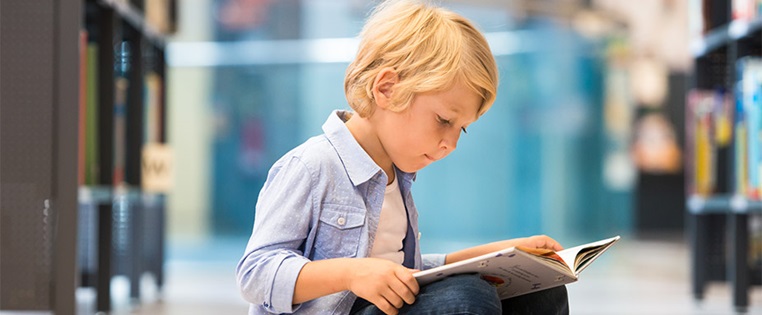 Junge ließt ein Buch in einer Bibliothek